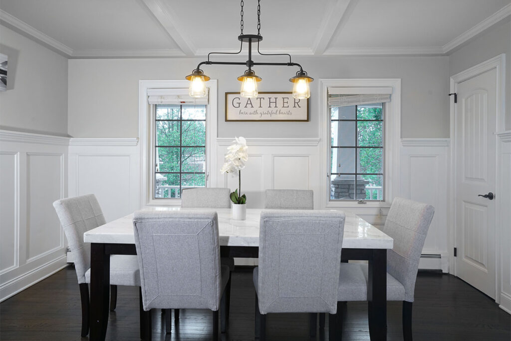 a dining room with a table and modern light fixture. a sign says "gather" on the wall