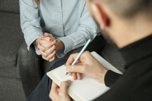 a therapist takes notes while talking to someone in one of their mental health treatment programs