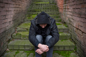 a person dealing with side effects of heroin sits with their head down on some outdoor stairs