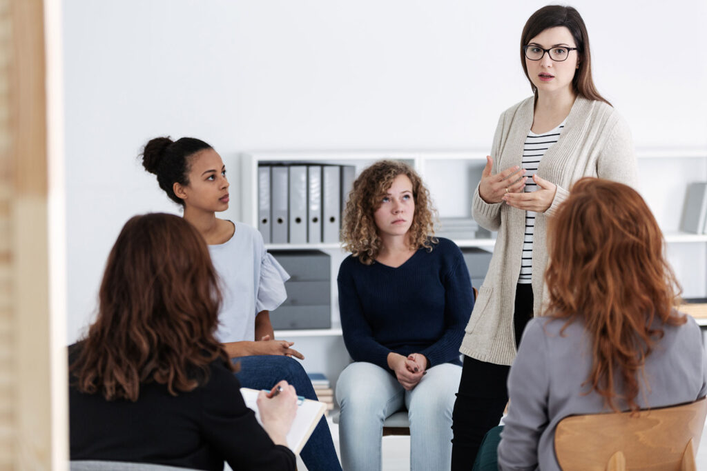 a group listens to a woman talk in a women's rehab program