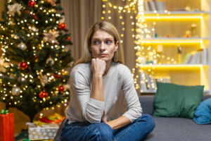 a person sits on the floor in front of a christmas tree wondering how to successfully stay sober for the holidays