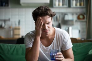 A man sitting on a couch, holding his head, visibly distressed due to alcohol withdrawal symptoms.